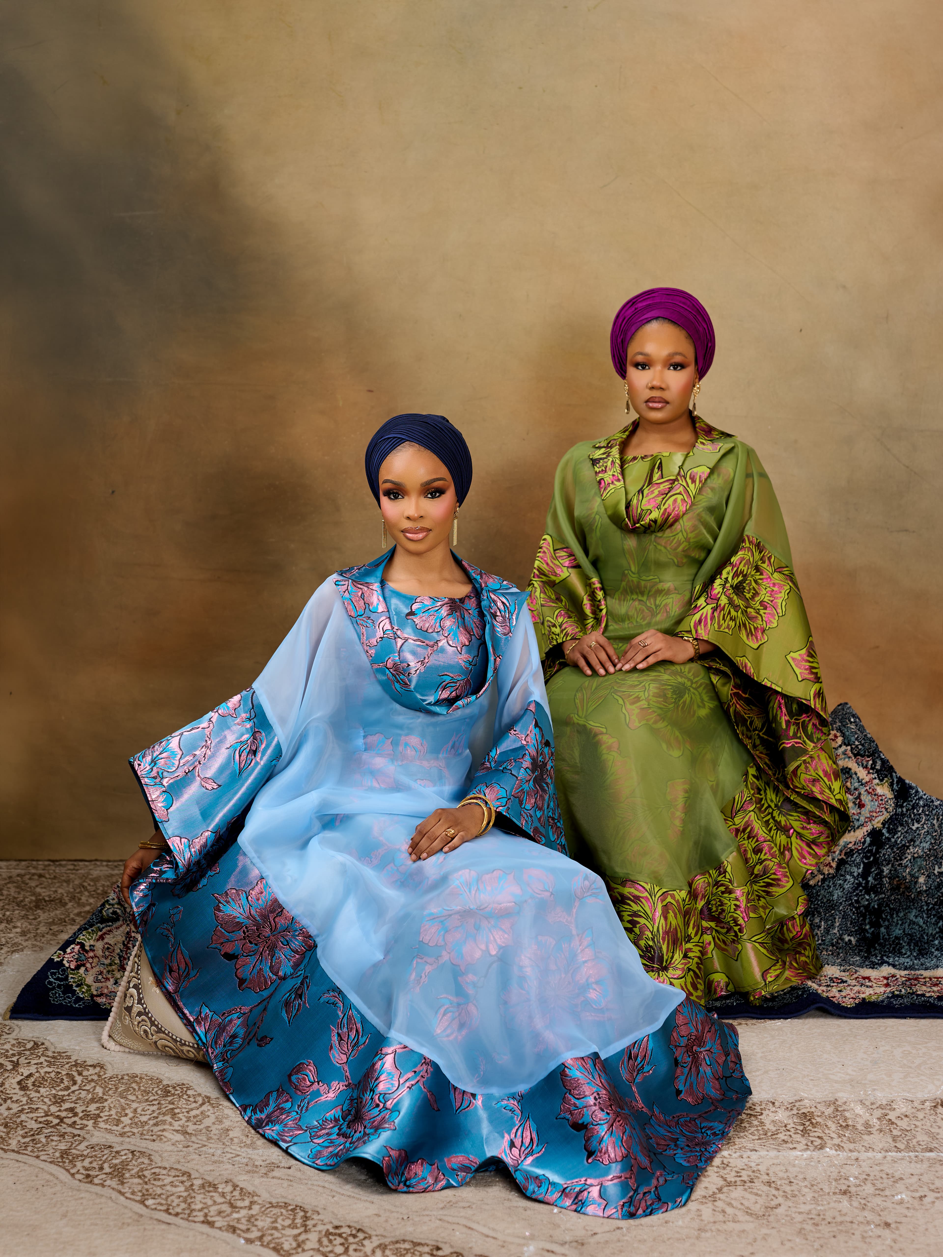 models in elegant blue floral and olive green gowns with vibrant headwraps against a warm, earthy studio backdrop
